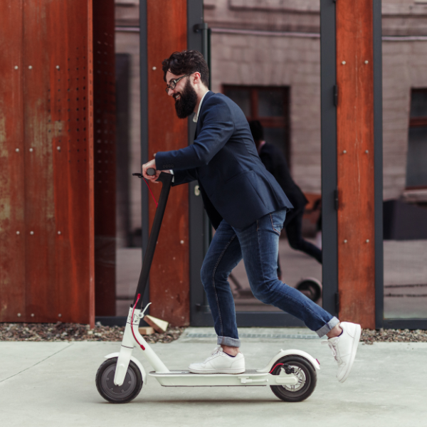 Bearded businessman riding to work on electric scooter
