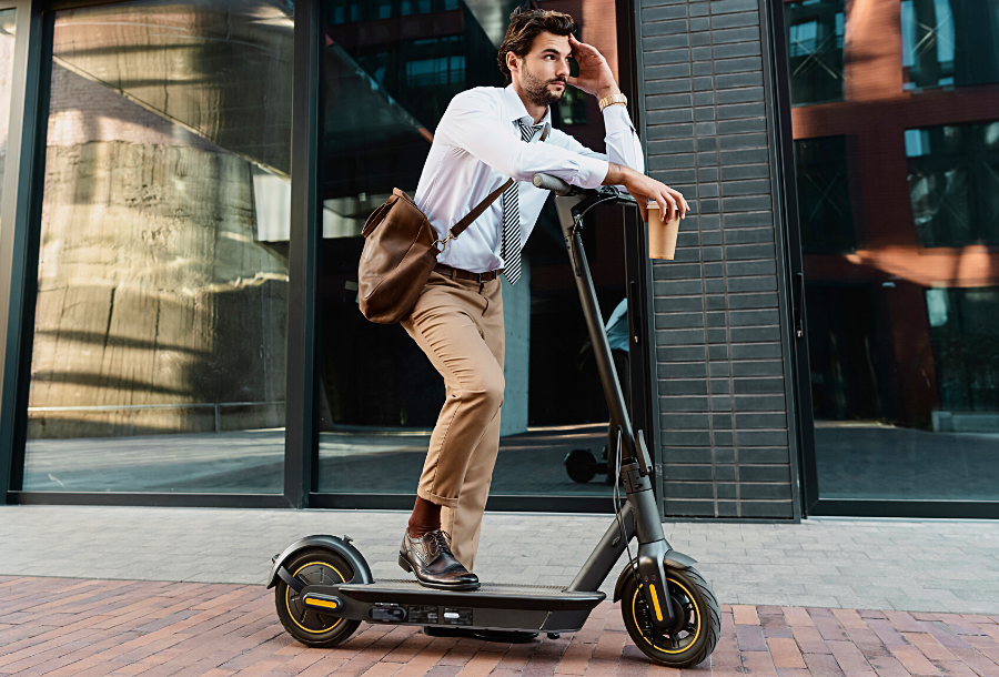 Man riding an electric scooter while holding a paper cup