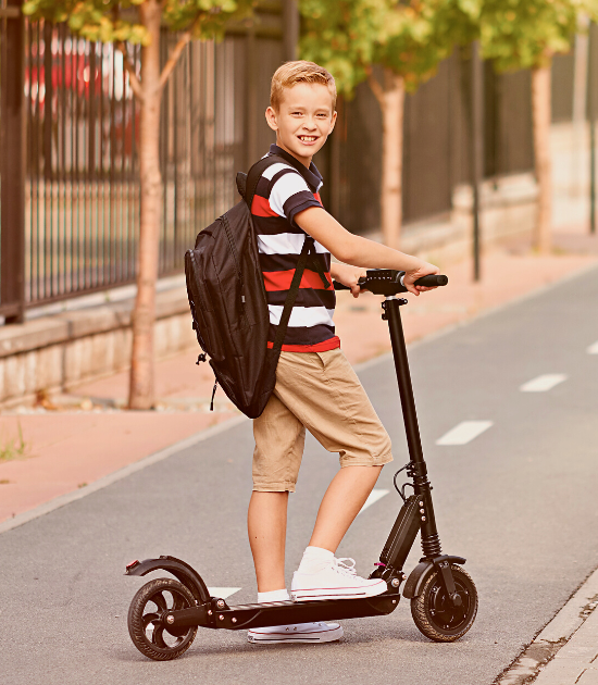 A young boy poses for a photo while riding his electric scooter on a road