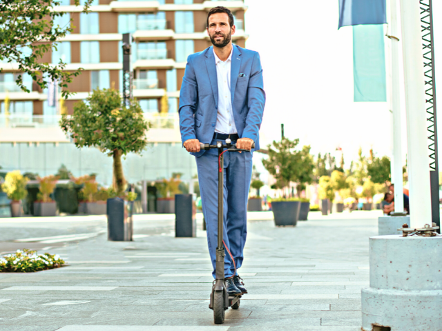 Young businessman in a suit riding an electric scooter