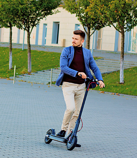 Man strolling the city with a Ninebot scooter, with trees can be seen on the background