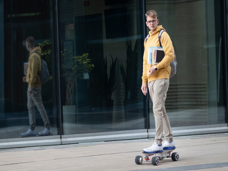 Student riding on electric urban modern skateboard with backpack, books and textbooks