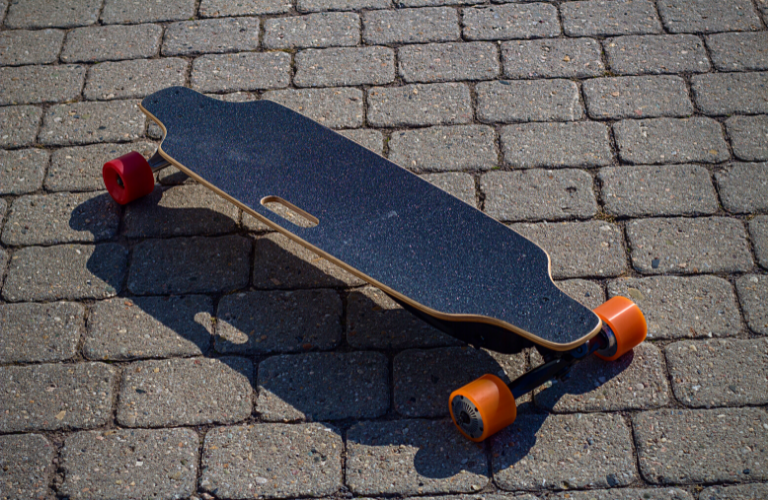 Image of black electric longboard with orange and wheels on pavers - My Electric Scooter