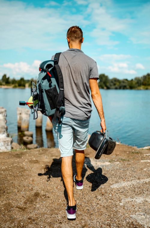 Young man with a backpack carrying a Onewheel Electric Skateboard near a body of water
