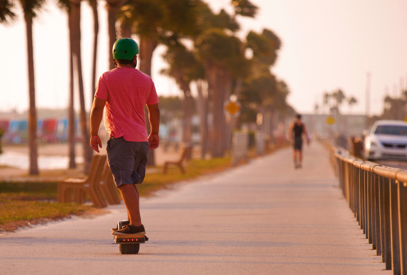 Man rides his onewheel electric skateboard on a boulevard near the sea