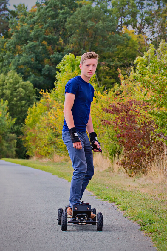 Young male traveler riding an electric skateboard on a road near the forest - My Electric Scooter