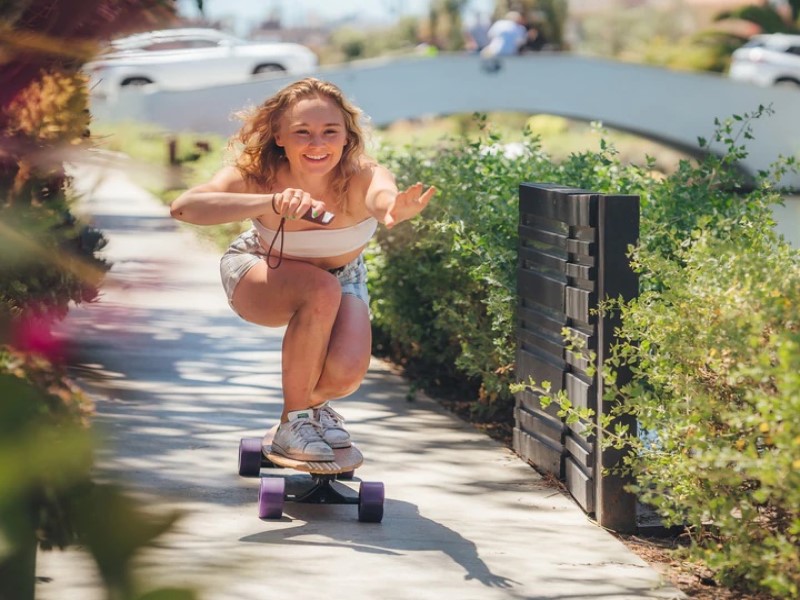 Woman rides an electric skateboard while holding a remote control