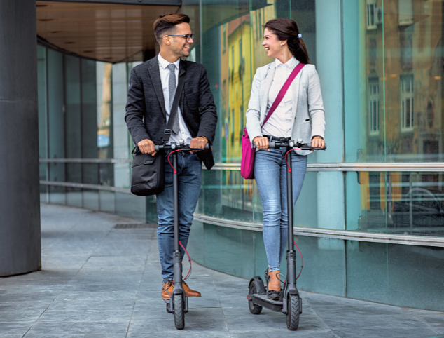 Two business partners driving electric scooter in front of a modern business building - My Electric Scooter