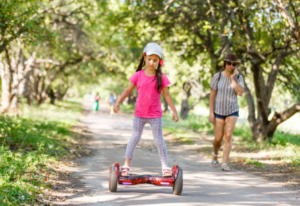 Young girl riding self-balancing electric hoverboard in park with people around - My Electric Scooter