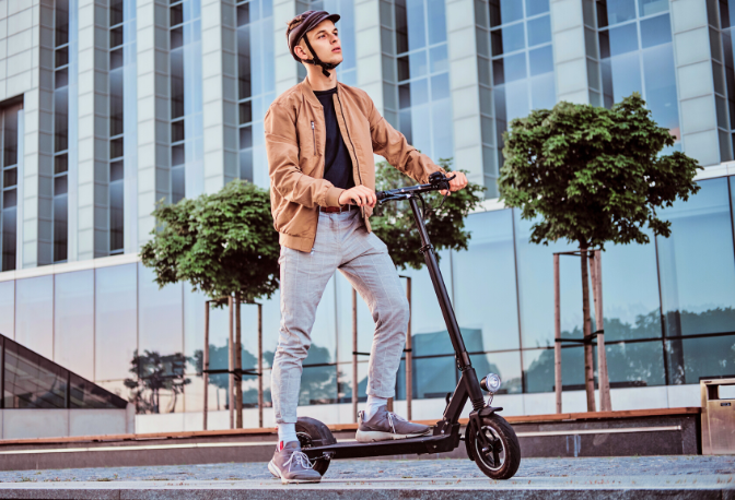 Man wearing a brown jacket riding an electric scooter on a road
