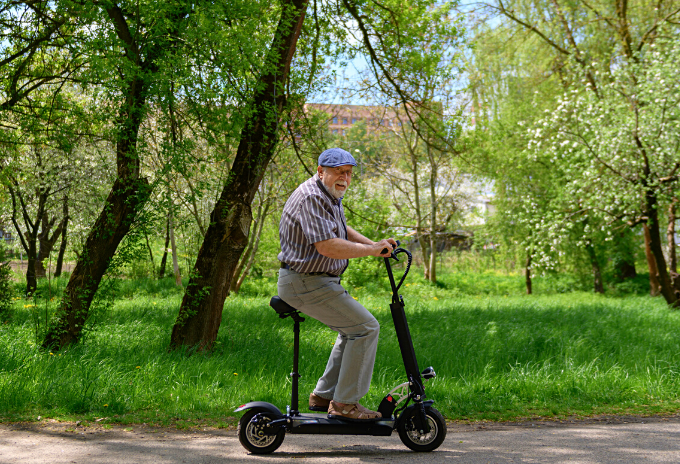 Old man riding an electric scooter on a park with lots of trees