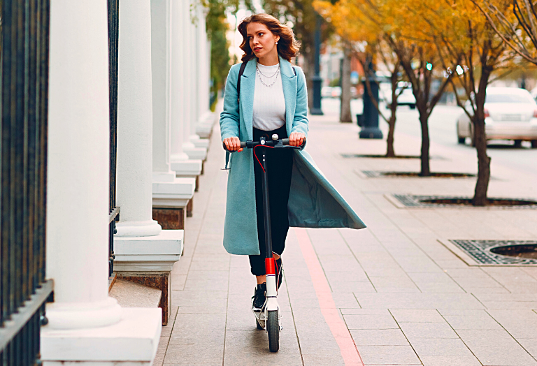 Stylish woman riding an electric scooter on the sidewalk