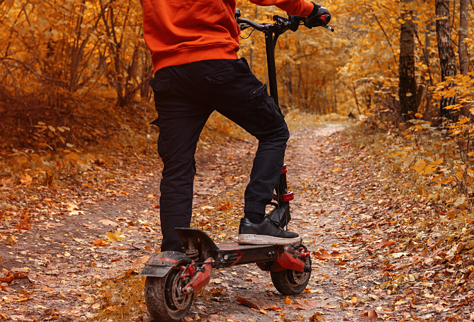 Cropped image of a person riding an all terrain electric scooter during autumn season, leaves scattered on the ground