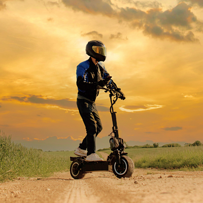 Man wearing a helmet riding an off road electric scooter on a dirt road