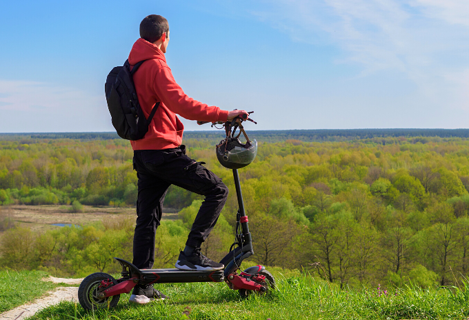 Man standing on a hill beside an electric scooter with large wheels