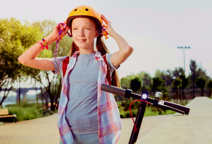 Young girl wears a helmet before riding an electric scooter