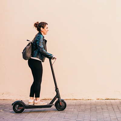 Side view of a woman riding an electric scooter on the sidewalk