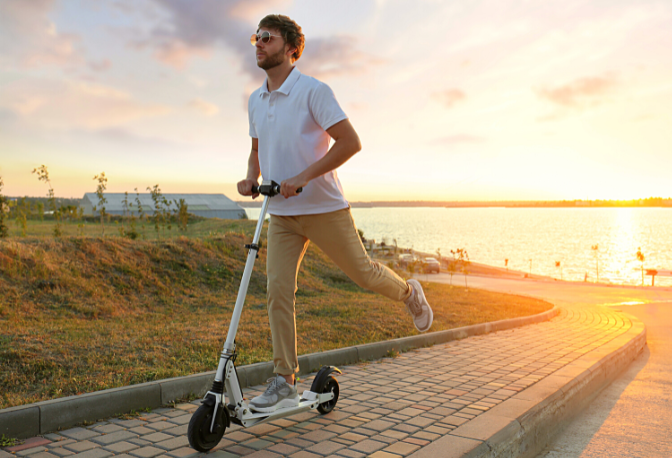 Man riding an electric scooter on a brick road during sunset