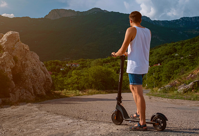 Man standing on an electric scooter on a road downhill