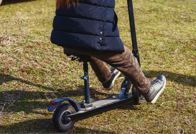 Cropped image of a person riding a seated electric scooter on a grassy field