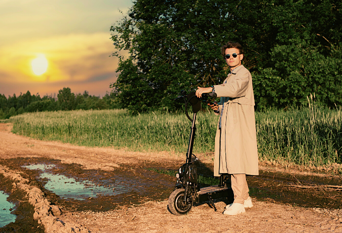 Man standing on a dirt road beside an electric scooter