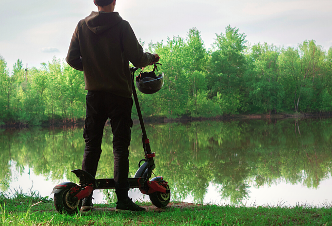 Man standing with his electric scooter near a lake