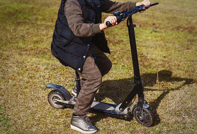 Cropped image of a person riding an electric scooter on a grassy land
